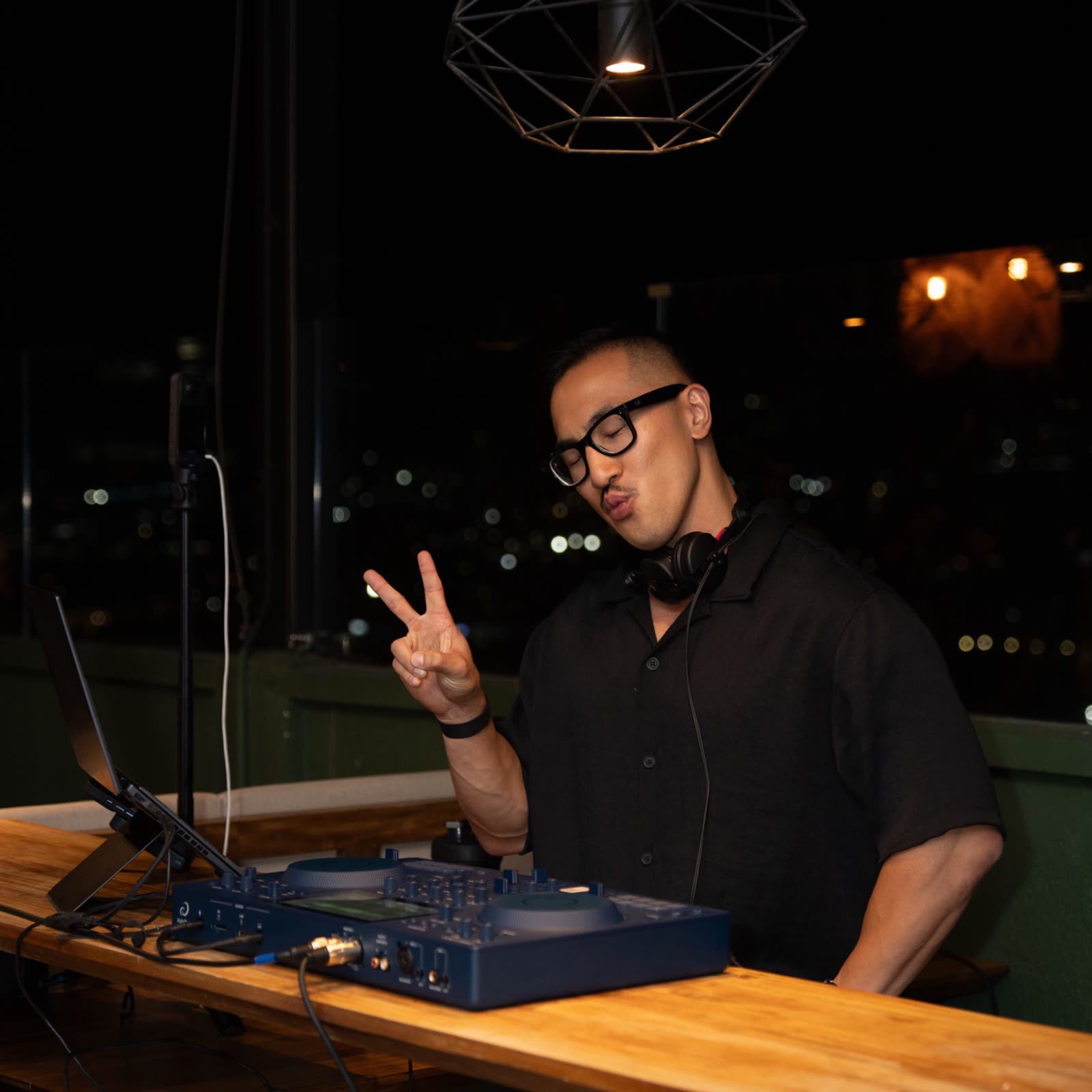 Sean Chi throwing a peace sign mid-set on a rooftop at night